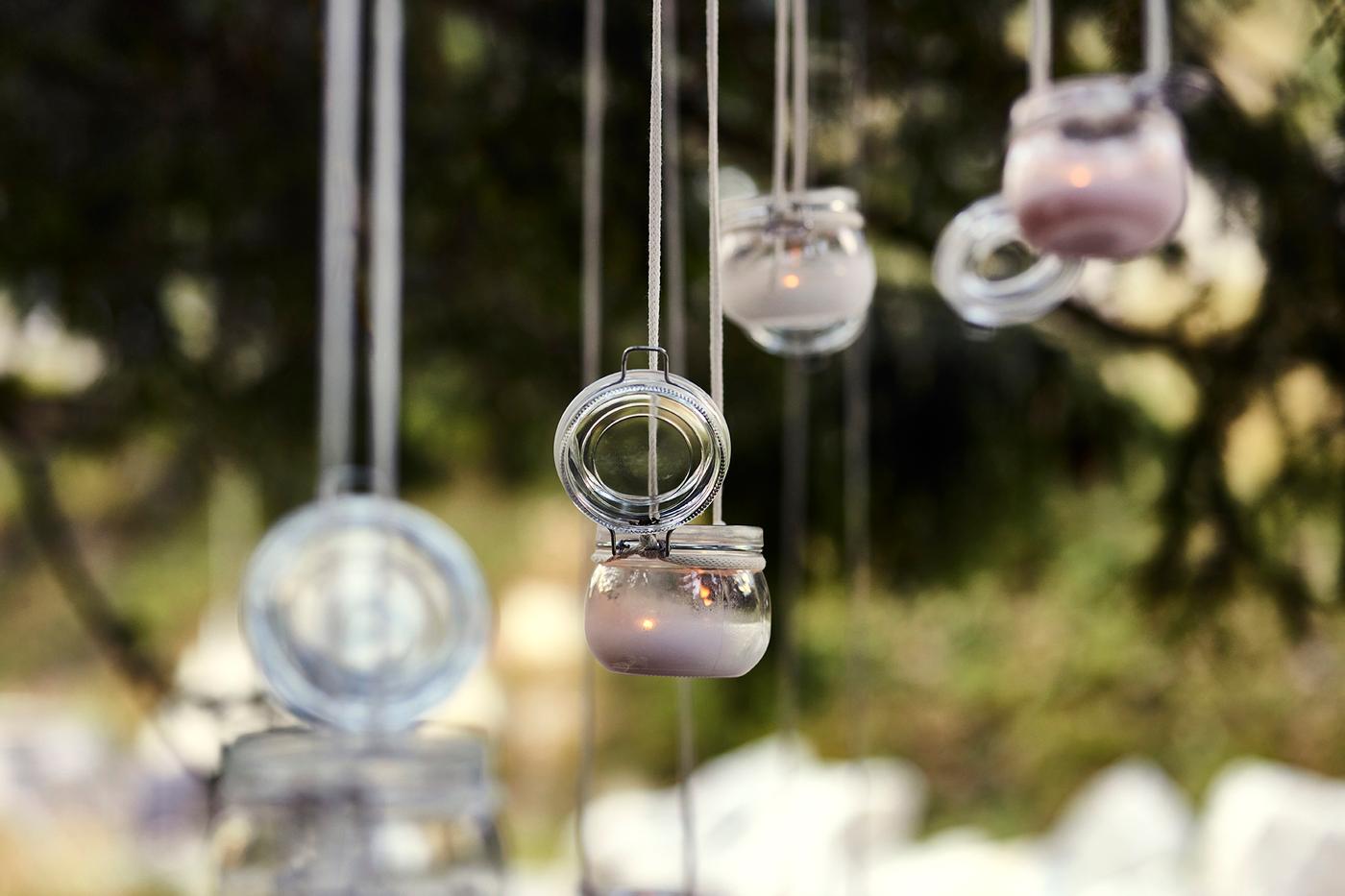 Hängende Glasbehälter mit Kerzen als stimmungsvolle Outdoor-Dekoration, im Hintergrund unscharfe Natur.