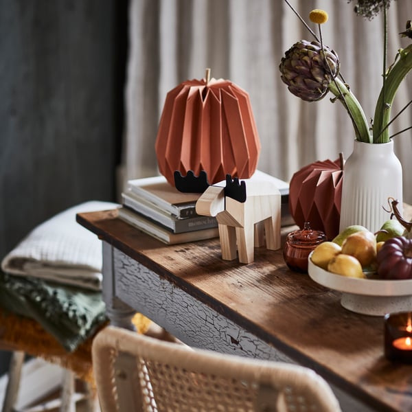 A rustic table adorned with HÖSTAGILLE 2025 decorations of a pumpkin and a moose, and a HÖSTAGILLE 2025 serving stand.