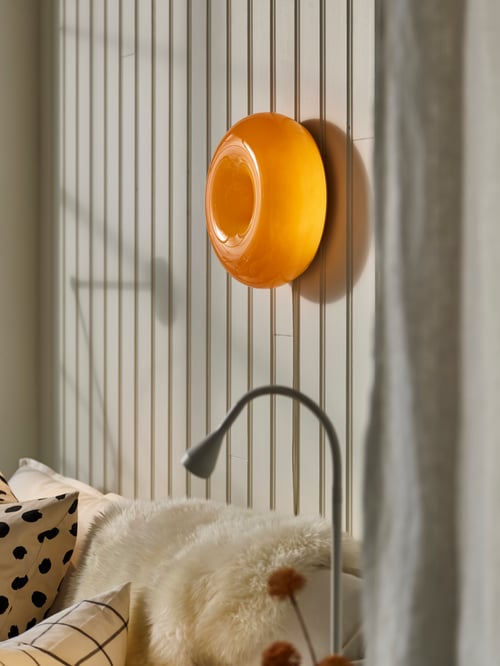 Living room focus of a LED table wall lamp shaped as a doughnut mounted on a wall above a sheepskin and 2 cushion covers.
