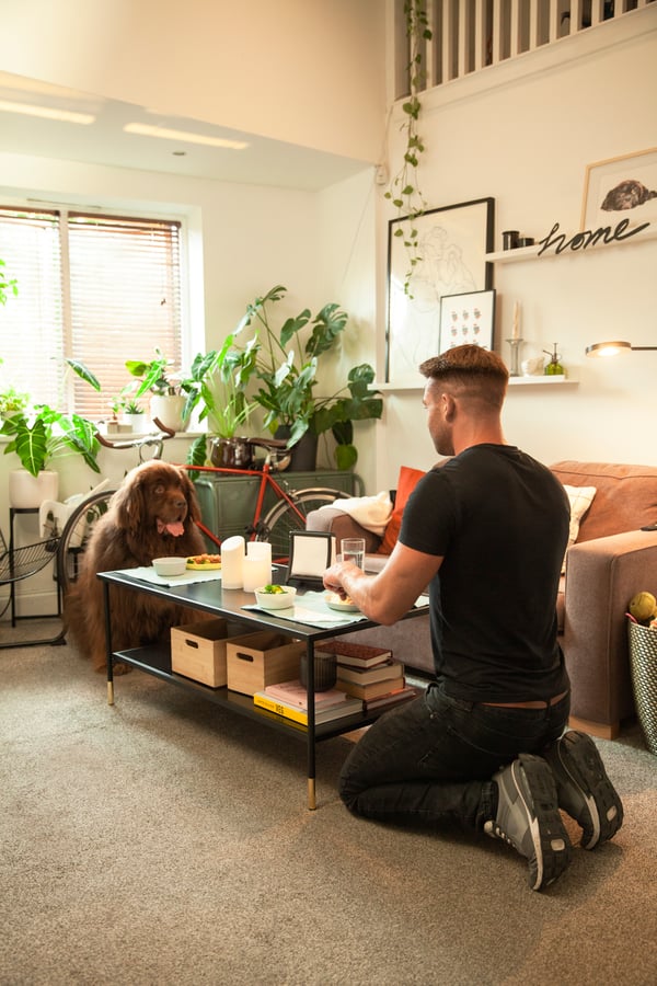 Un homme et son chien sont assis à une table basse dans le salon et prennent un repas.
