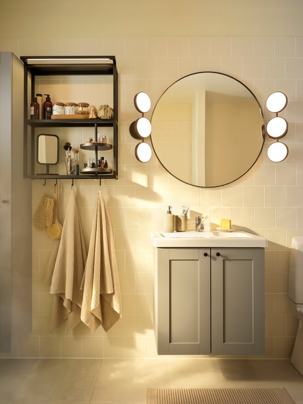 Boho deco style bathroom with grey sink unit and round bathroom mirror with LED wall lamps above.