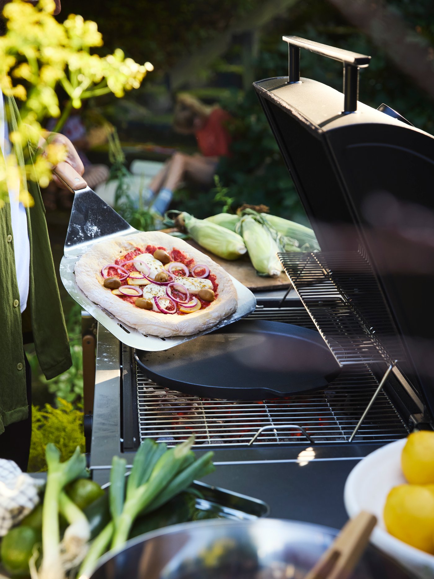 Making a homemade pizza on the BÅTSKÄR barbecue in the garden, using GRILLTIDER pizza shovel and pan for a perfect finish.