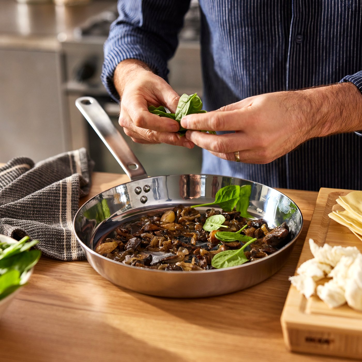 Miehen kädet ripottelevat yrttejä HEMKOMST-paistinpannulla olevaan ruokaan.
