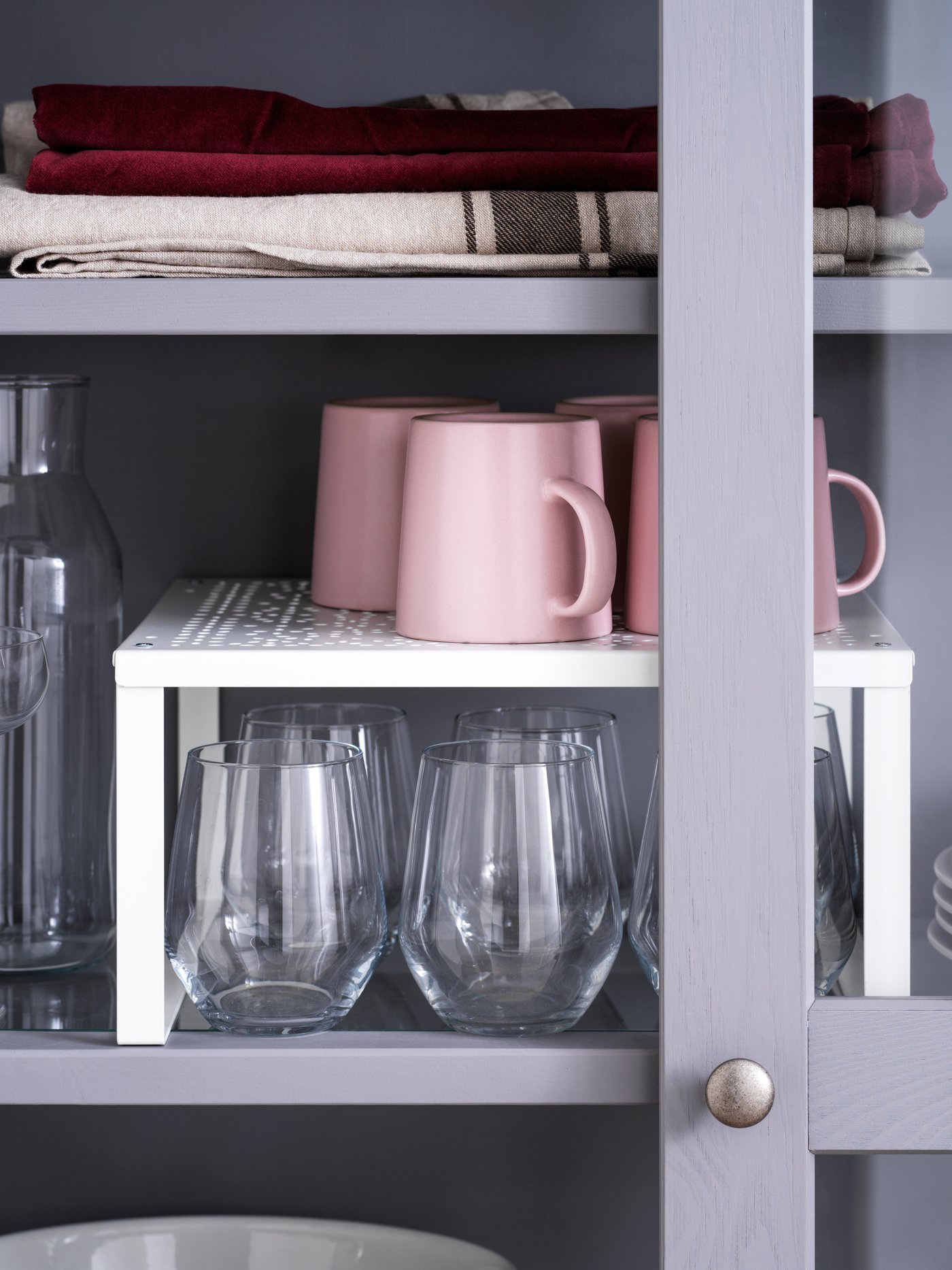 Detalle de un estante adicional blanco de acero con varias tazas rosas encima de vasos blancos, en una cocina.