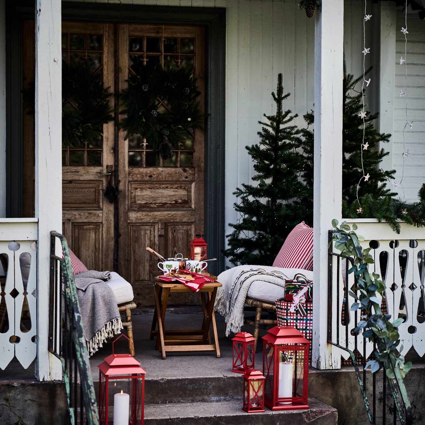 Ein Tischchen mit Teetassen und zwei Stühle mit rot/weiß gestreiften VINTERFINT Kissen und Decken auf einer winterlichen Veranda.