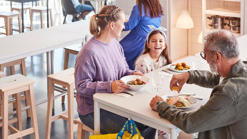 Ein Mann und eine Frau sitzen zusammen mit einem Kind im IKEA Schwedenrestaurant und essen.