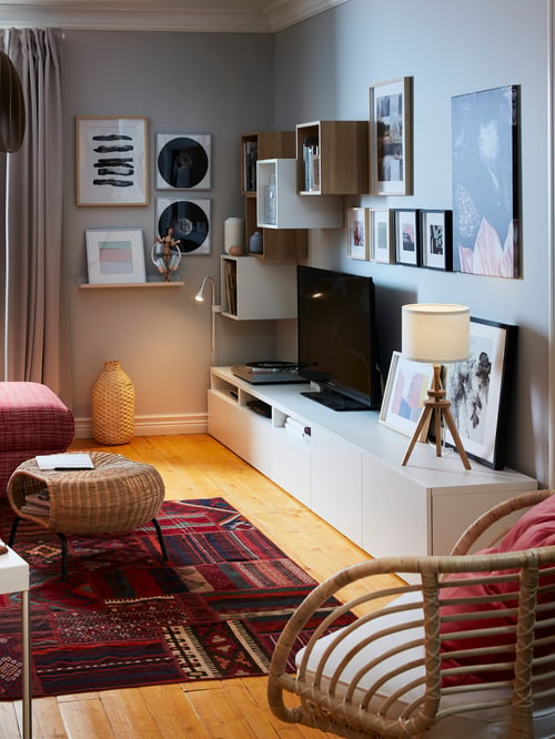 Un salon dans lequel on retrouve une armoire où se trouvent une télévision et une lampe de table, un fauteuil, un repose-pieds avec rangement et un tapis.