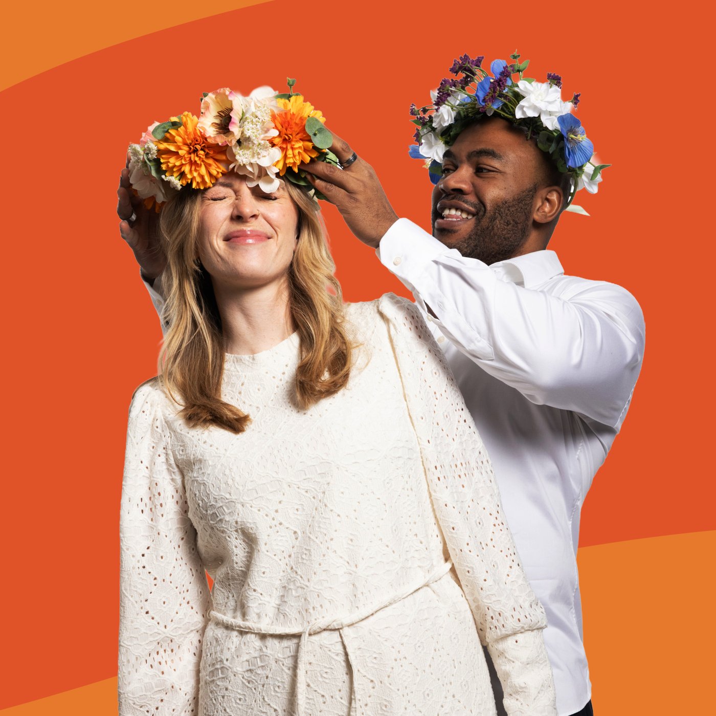 A persona places a colourful flower crown on the head of another who is standing in front, both against an orange background.