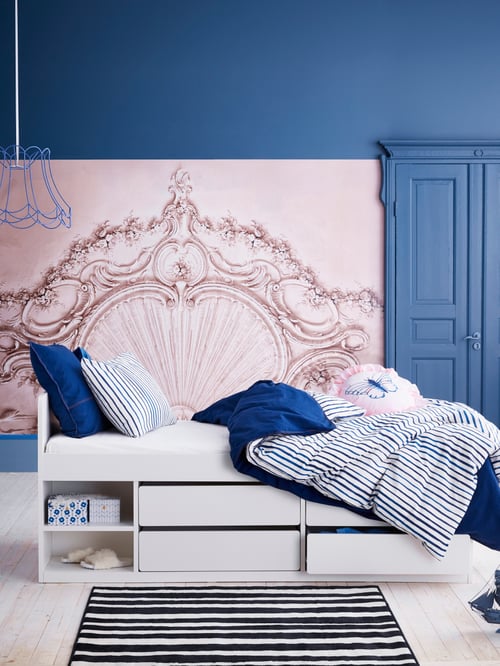 Bedroom with Navy blue walls, blue pendant, white bed frame with storage, quilt cover and pillowcases, boxes with lids, rug.