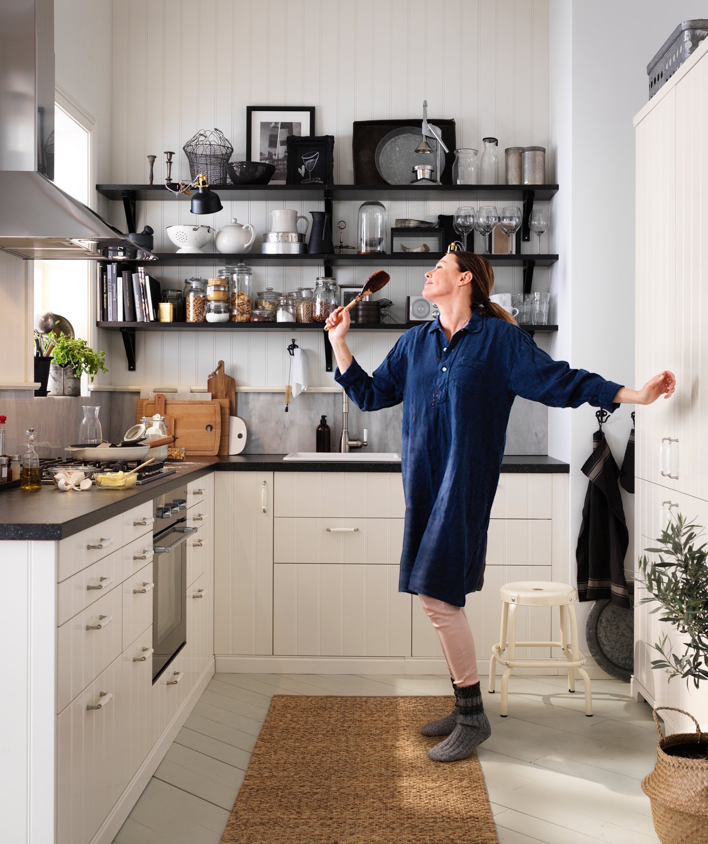 Girl singing and dancing in the middle of L shaped kitchen with white cabinets and black countertops