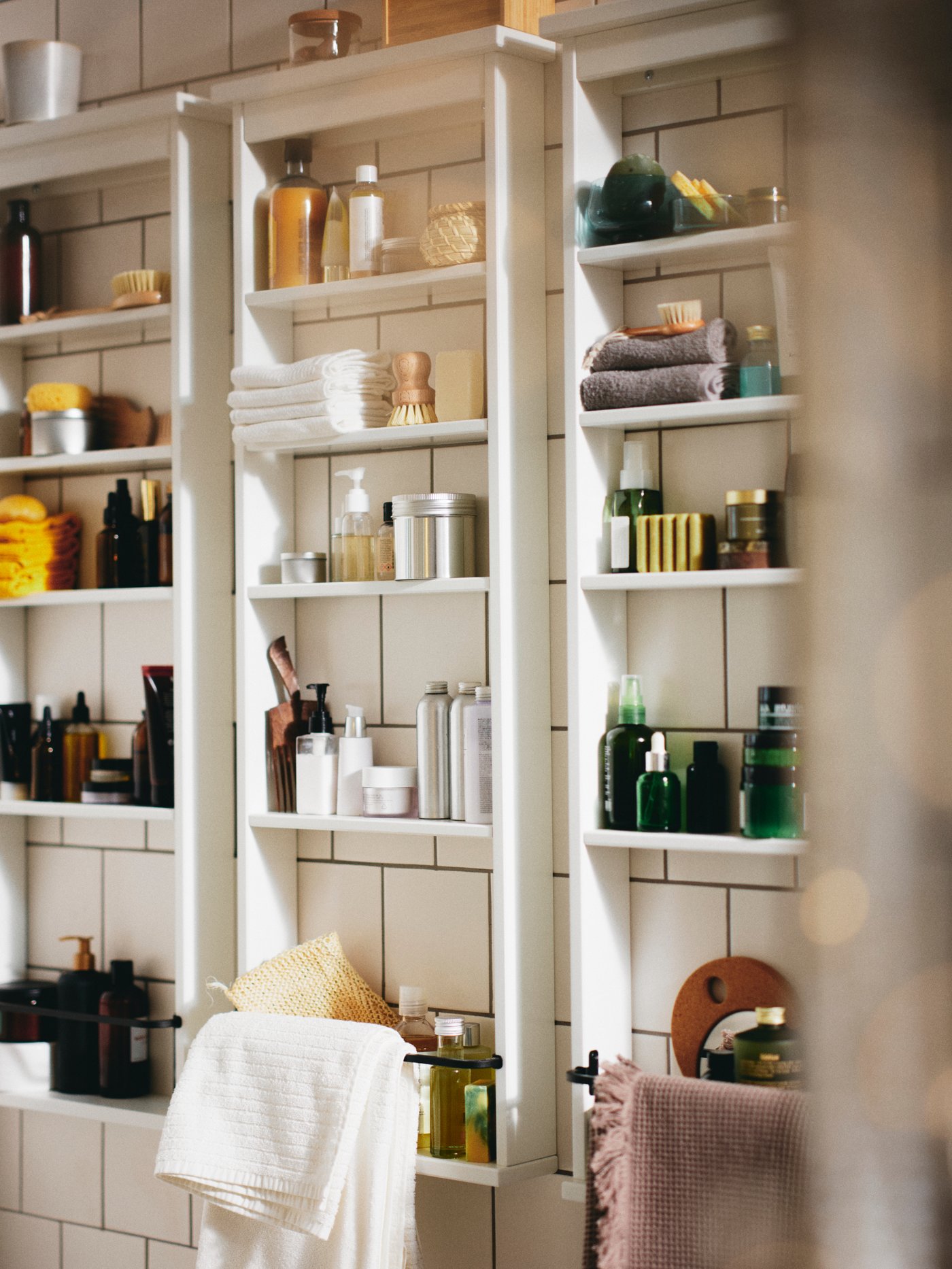 A wall with three white HEMNES wall shelves filled with products and a white VÅGSJÖN bath towel.