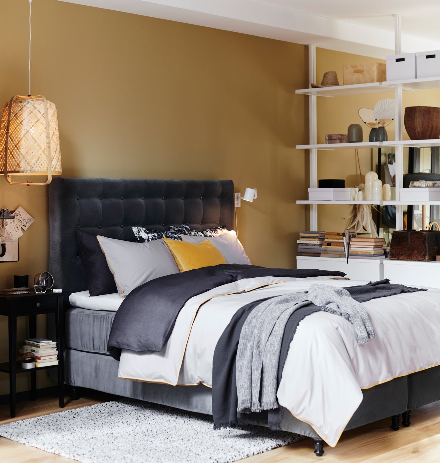 Ein Bett mit einem grau gesteppten Kopfteil und Bettwäsche in verschiedenen Schichten