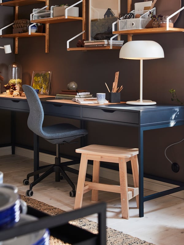 Two blue desks, a wall-mounted shelf combination in bamboo, a white table lamp and a birch stool.