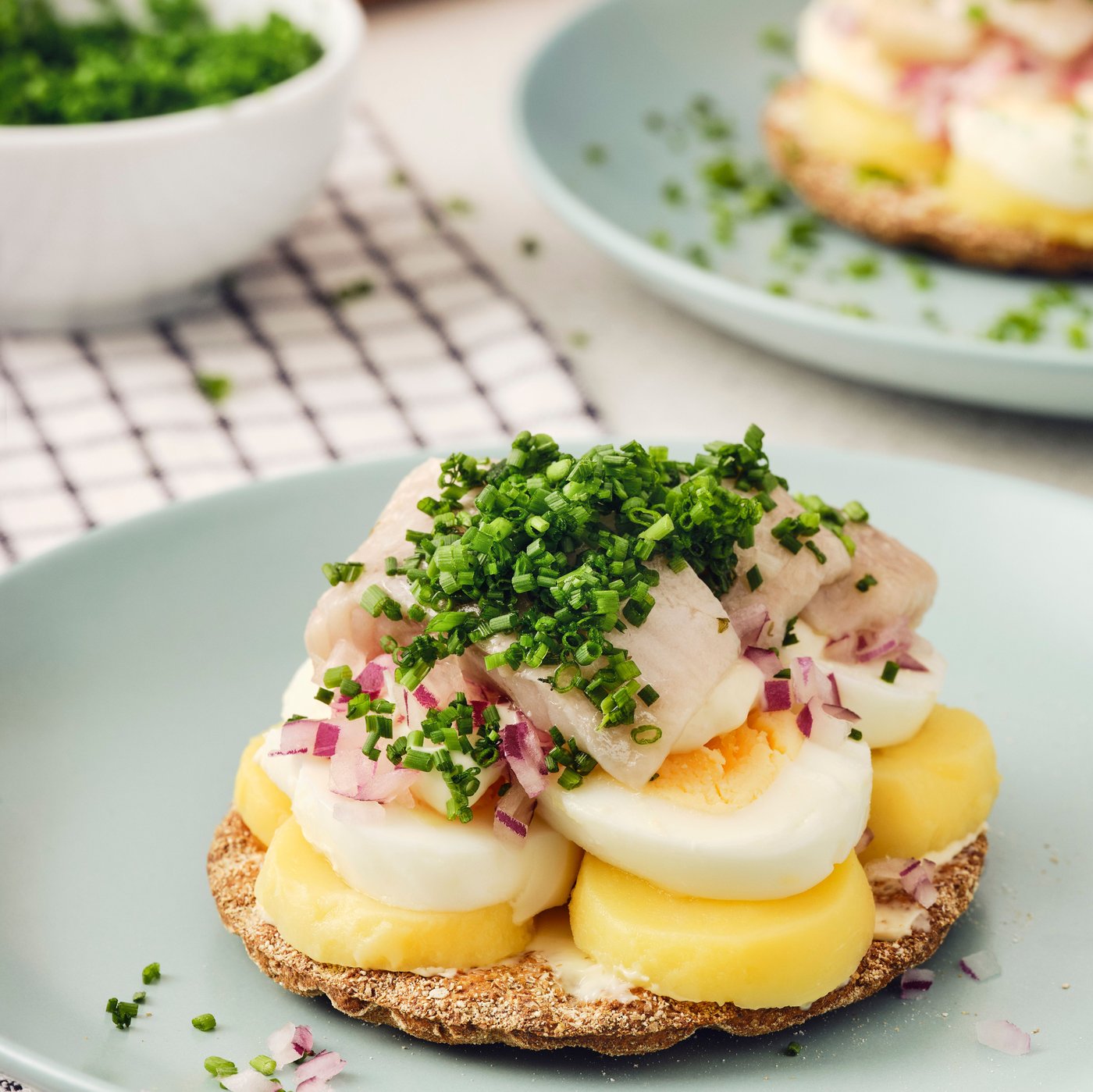 An open KNÄCKEBRÖD RÅG rye crispbread sandwich with eggs, SILL DILL marinated herring, and chives on a green plate.
