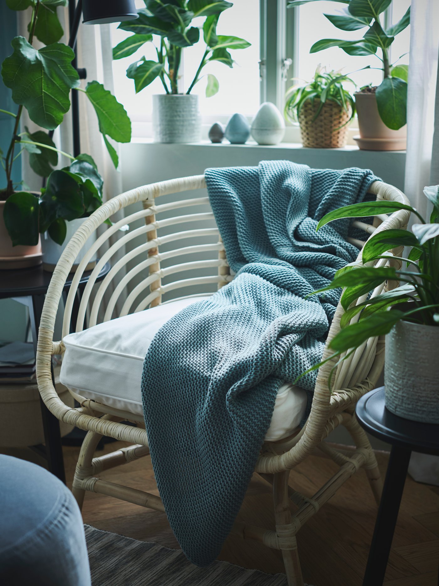 A BUSKBO armchair with a pale blue INGABRITTA throw is surrounded by potted plants in front of a bright window.