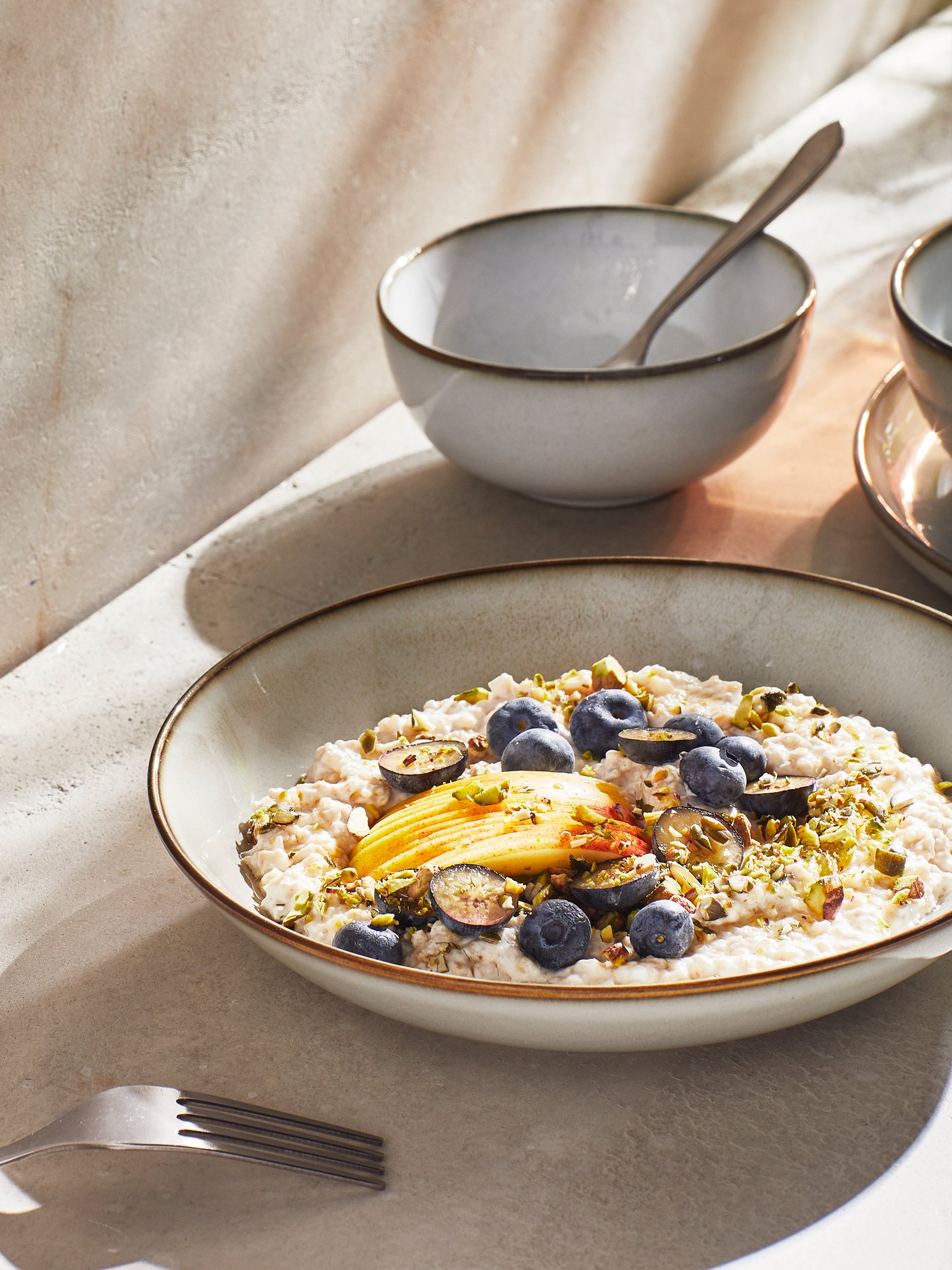 Piatto fondo GLADELIG grigio riempito di porridge con frutta fresca su un tavolo illuminato dalla luce naturale, accanto a una ciotola coordinata.