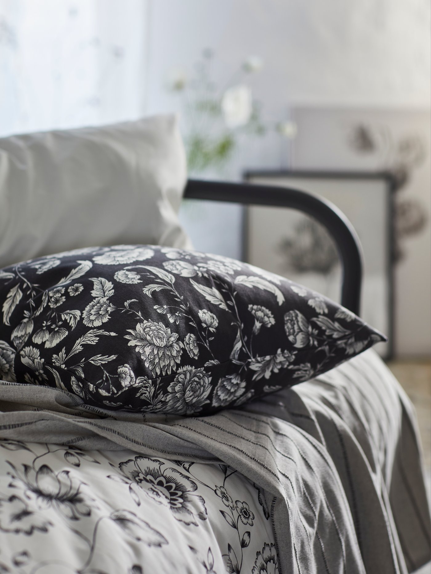 JUNGFRUNAVA duvet cover and pillowcase on a FYRSSEDAL bed frame with an IDALINNEA cushion cover in black and white florals on top of it.