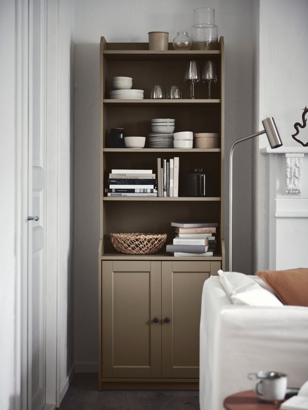 A light living-room corner with a beige HAUGA two-door high cabinet holding books, tableware and decorations.