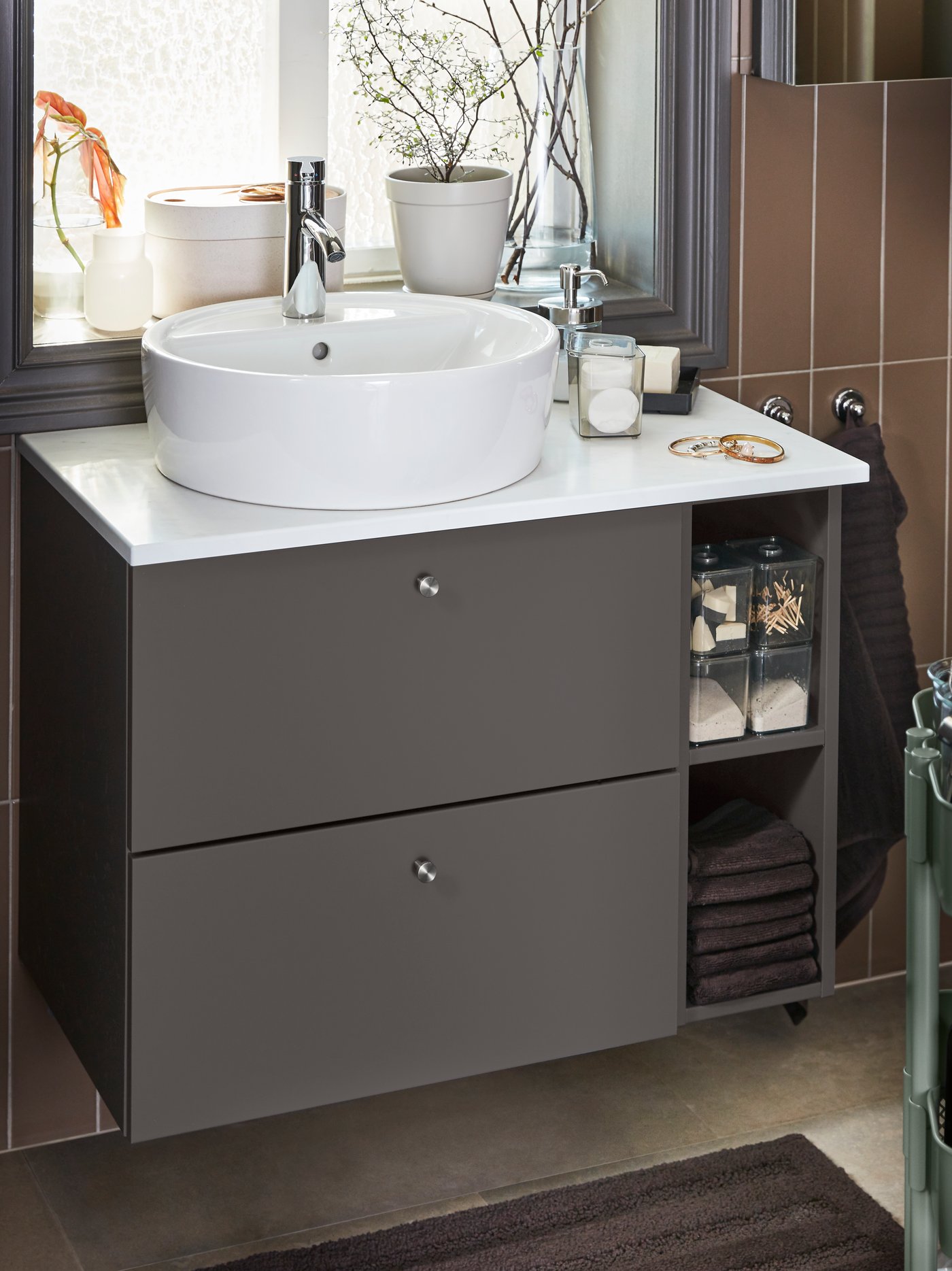 A wash-stand/wash-basin in dark-grey/white, towels and a bath mat in dark-brown.