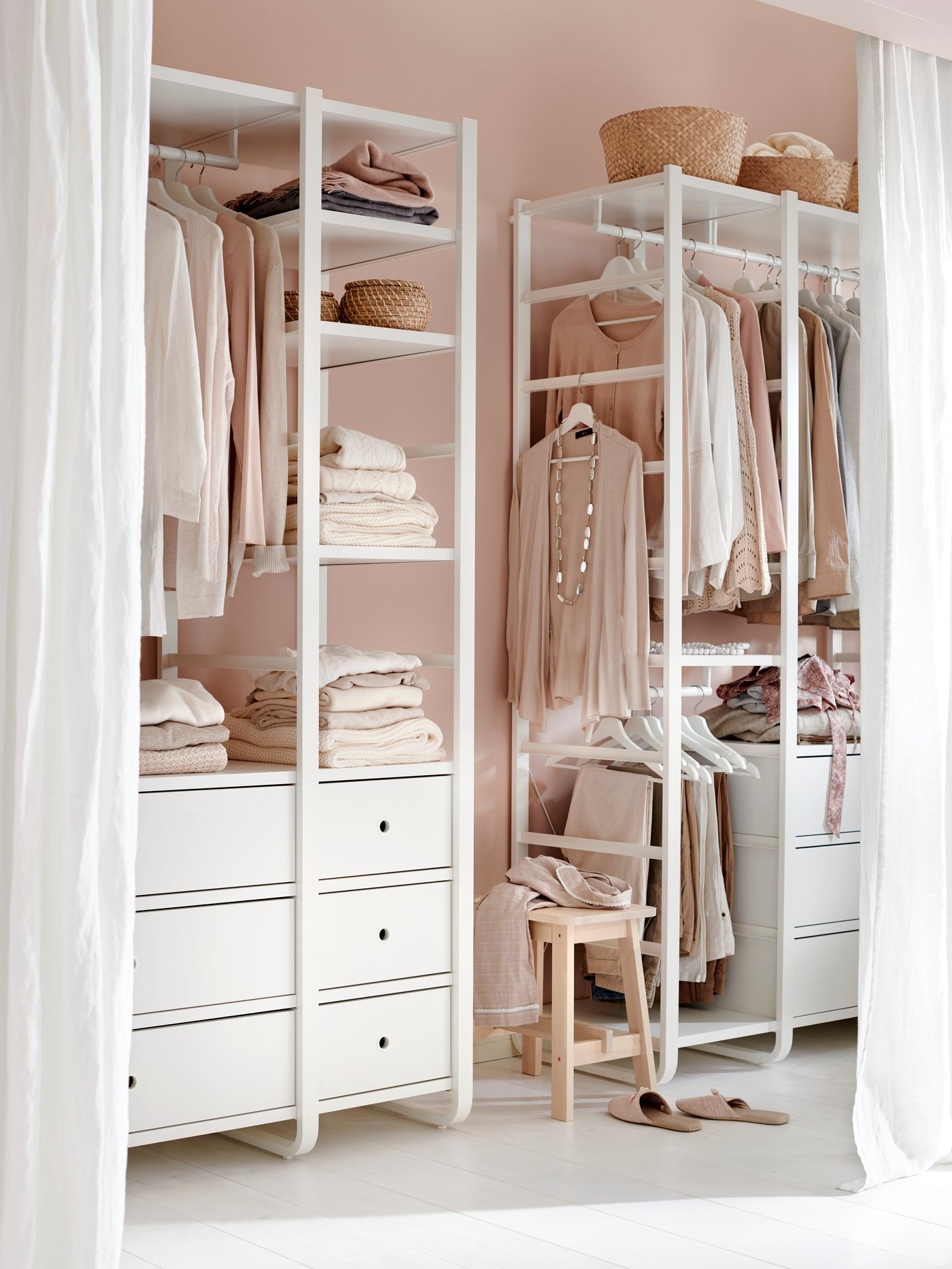 Vita garderobslösningar står framför en rosa vägg, bakom ett drapperi.