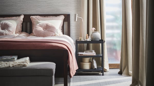 IDANÄS pink upholstered bedframe in bedroom with open and airy feel paired with pink sheer curtains, wood bedside table and white furniture.