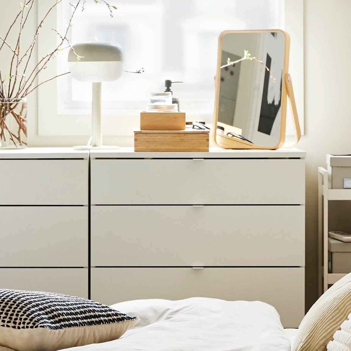 A bedroom with two white VIHALS chests of 4 drawers, featuring decorative items and a table lamp, next to a large window.