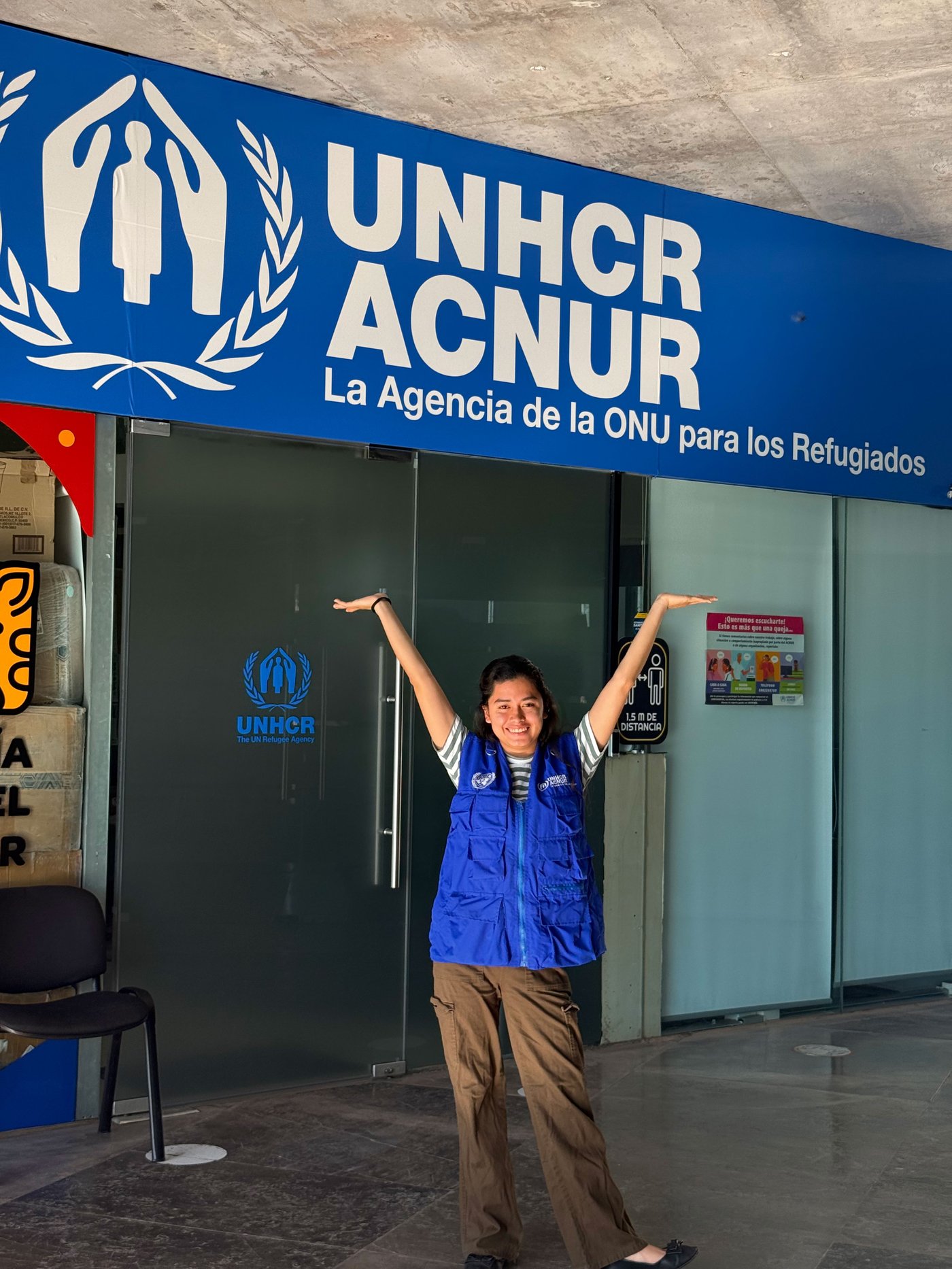 Natalie outside a UNHCR office smiling with her arms up in the air.