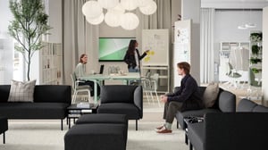 Un jeune homme assis dans un coin salon avec plusieurs canapés modulaires LILLEHEM gris foncé, des tables TUNSTA et un coin réunion derrière.