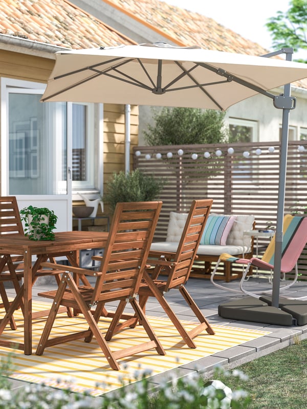 Un juego de comedor para exterior NÄMMARÖ con cuatro sillas reclinables de madera. Sobre el comedor hay un toldo SVALÖN.