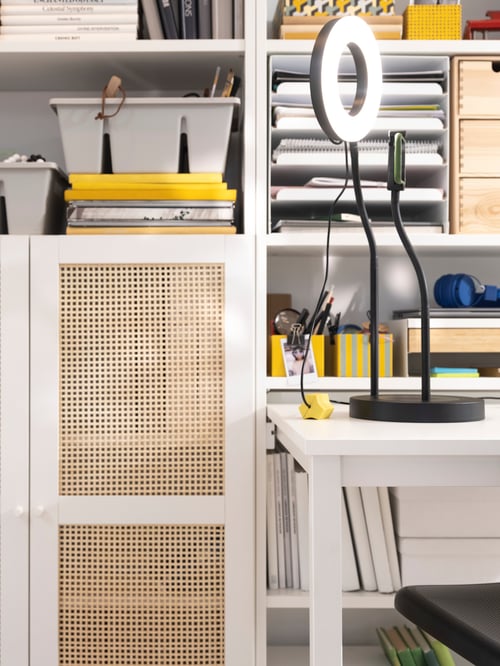 A workspace featuring HÖGADAL doors placed on a white cabinet, next to a desk with an USB anchor and a lit ring light on top.
