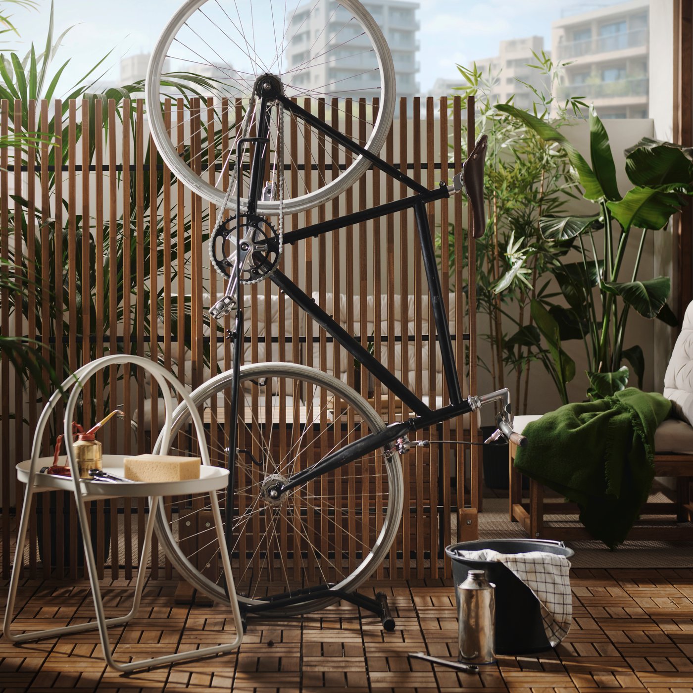 A lush city balcony features a light brown stained NÄMMARÖ privacy screen, surrounded by outdoor furniture and a bike.