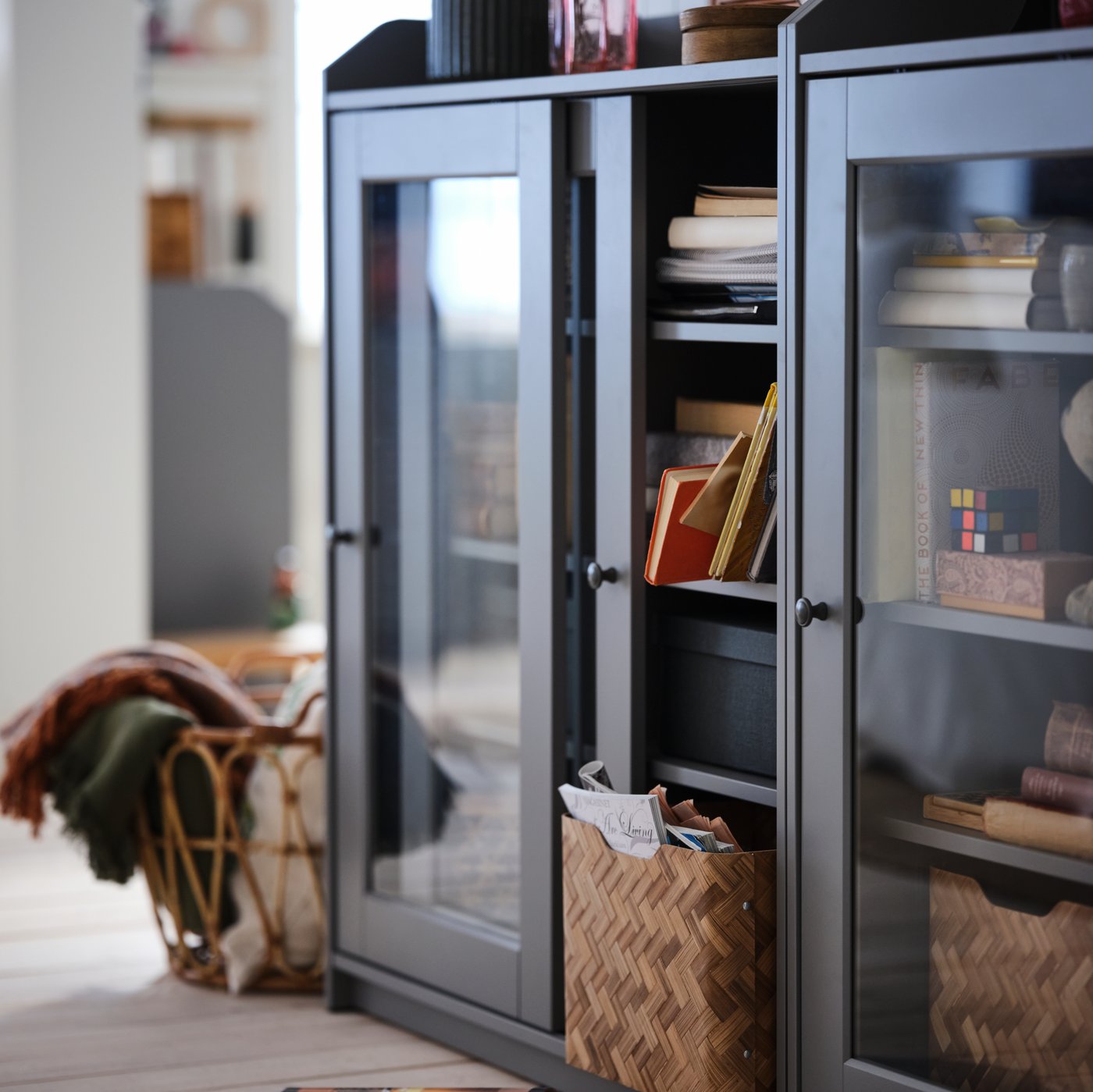 A wooden-floor room with a grey HAUGA glass-door cabinet filled with everyday storage inside and decorative items on top.