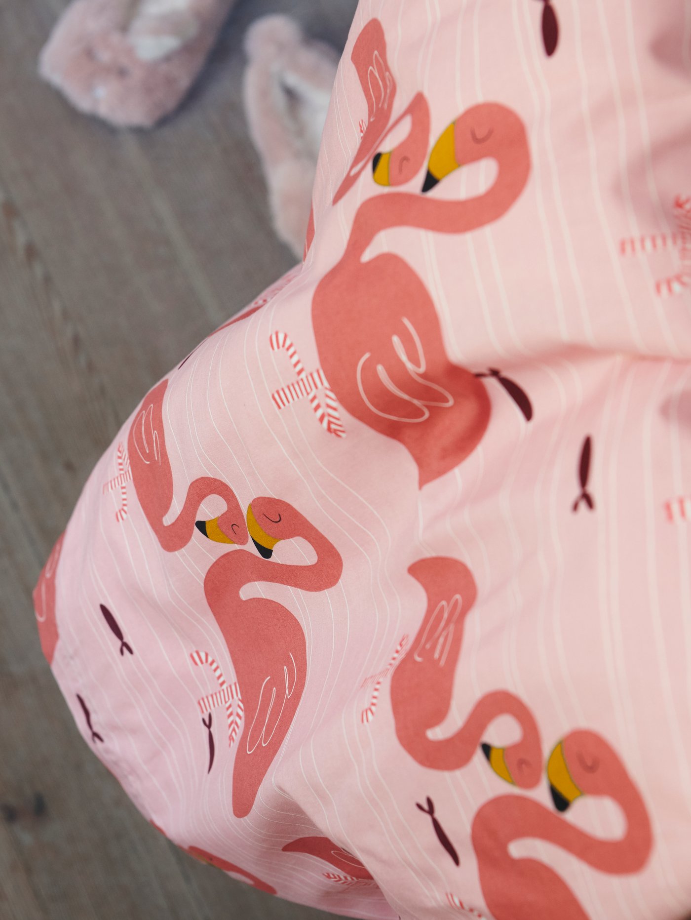 Prikaz papuča na podu pored RÖRANDE popluna za krevetić s uzorkom na plamence.