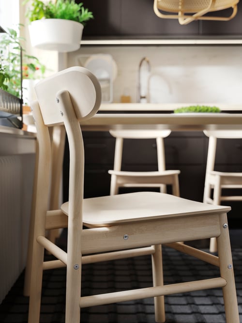 A beige chair in the foreground with two other out of focus chairs and a base cabinet in the background.