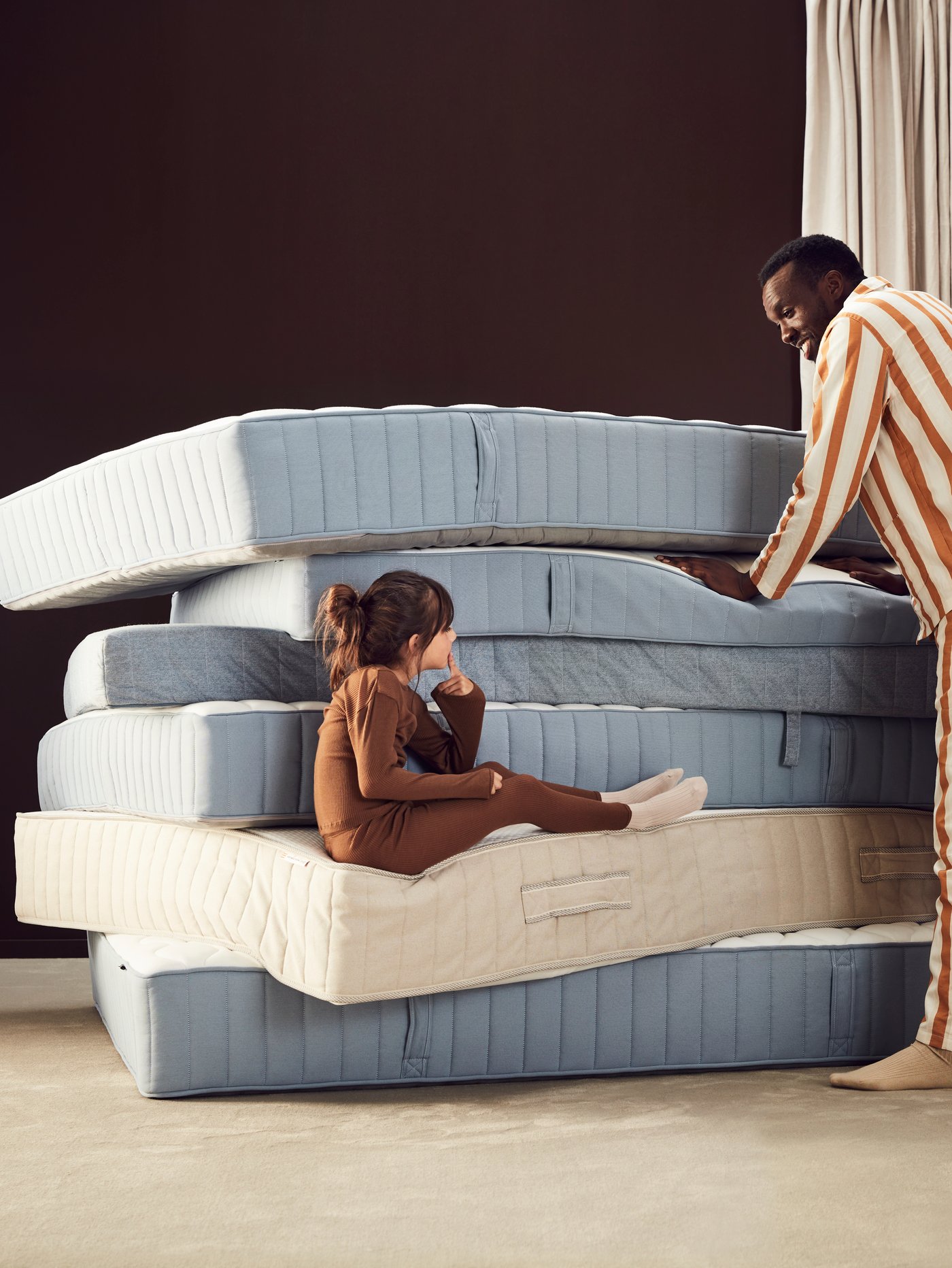 Una rumba de colchones en una habitación y una niña sentada en una esquina con el padre al costado.