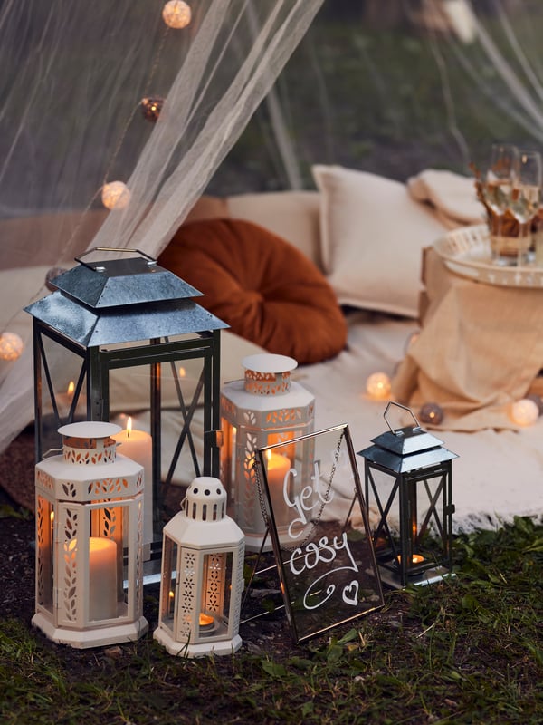 Outdoor area with candles lit in various lanterns near a draped seating area on the floor.