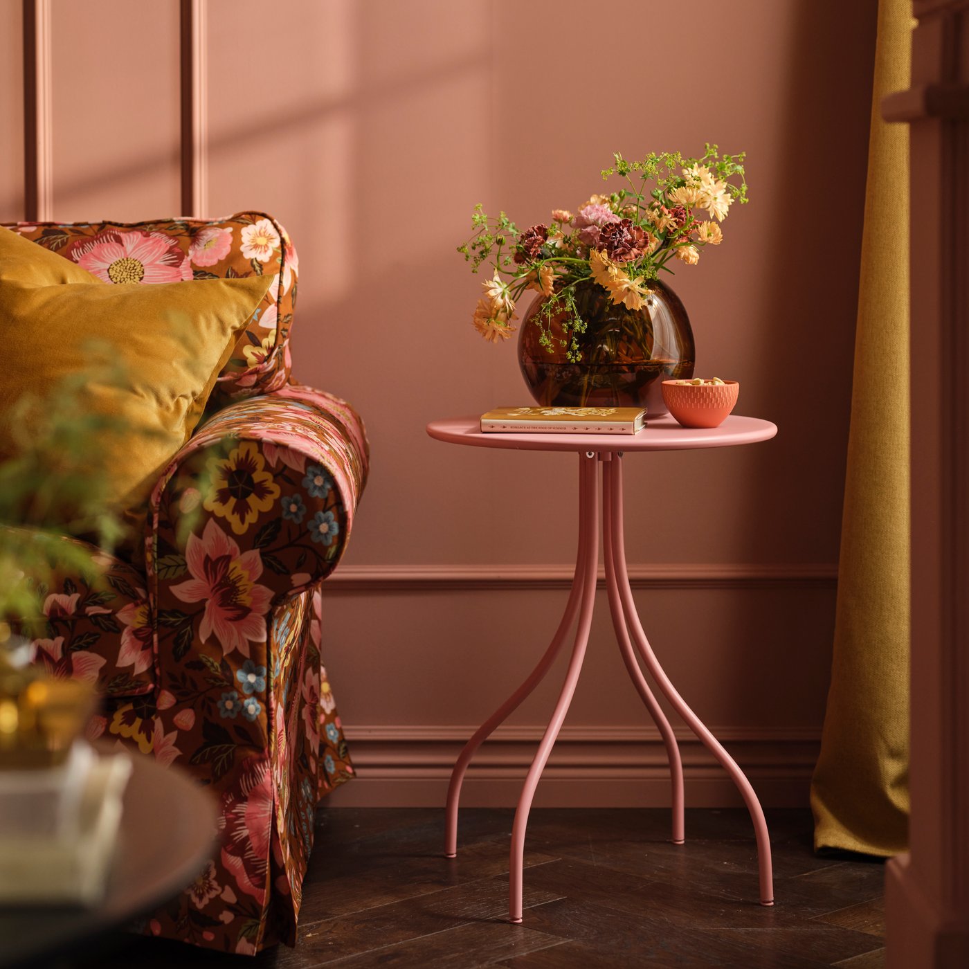 A TÅNEBRO side table in light pink stands in a pink living room next to an EKTORP sofa with a floral sofa cover.