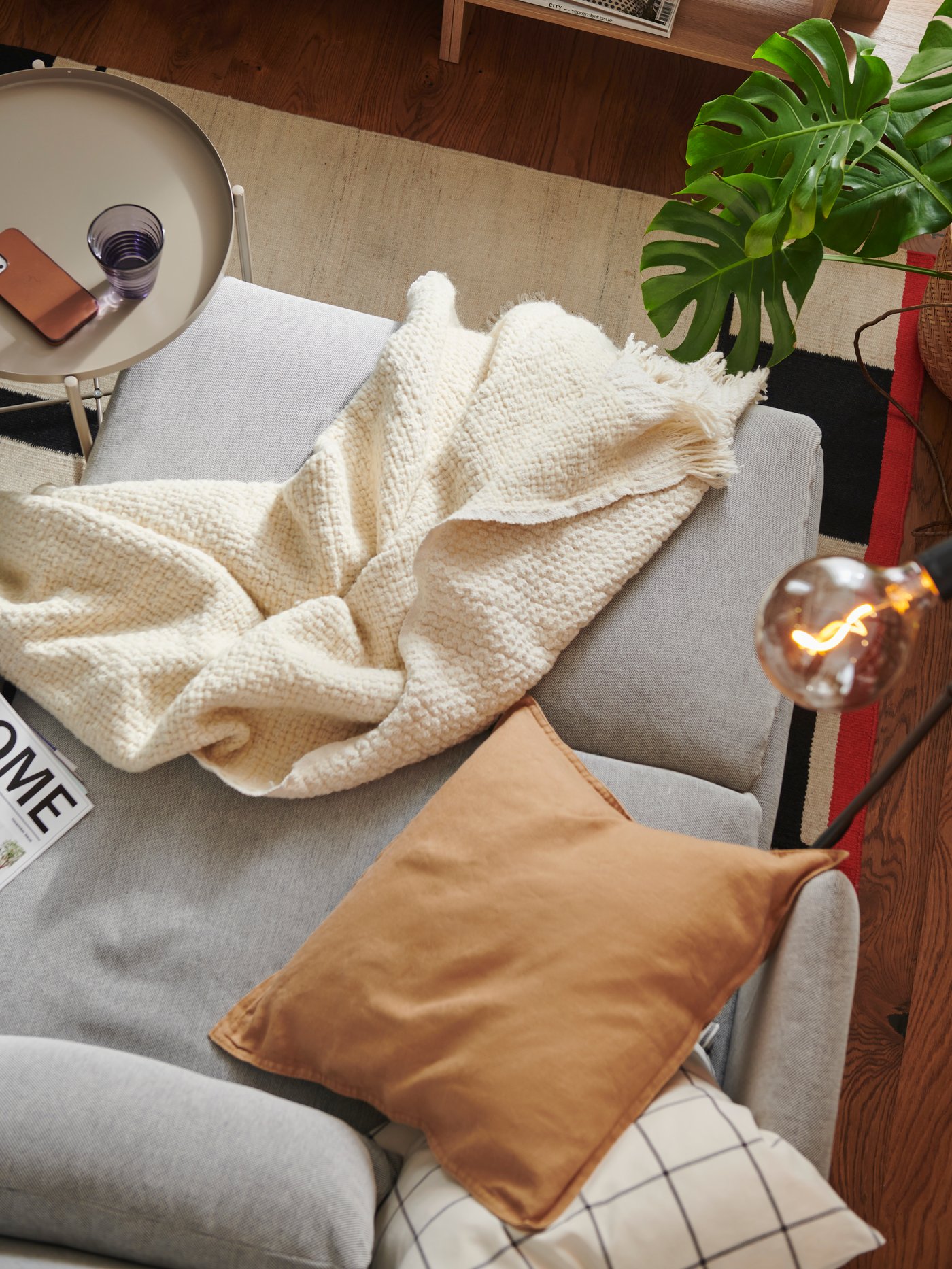 Dettaglio visto dall’alto di un divano grigio chiaro in un soggiorno decorato con plaid, coperte e cuscini a tinta unita e fantasia geometrica.