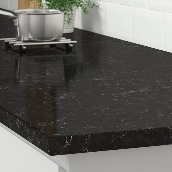 The corner of a LOCKEBO black marble effect countertop on a white kitchen cabinet with a stainless steel pot on a trivet.