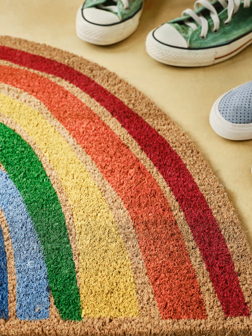 A modern hallway that features an indoor door mat with a rainbow pattern next to two pairs of sneakers.