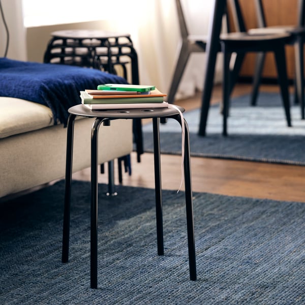 A room with LISABO chairs and a MARIUS stool in black with a number of books placed on it on a blue rug.