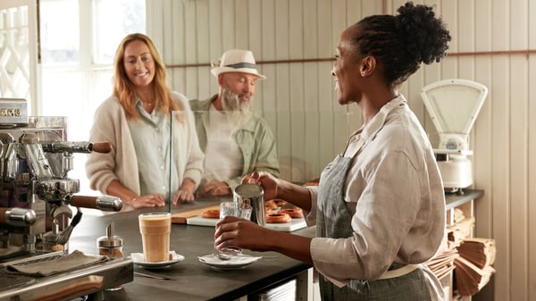Una donna serve il caffè a due persone al bancone di un'accogliente caffetteria.