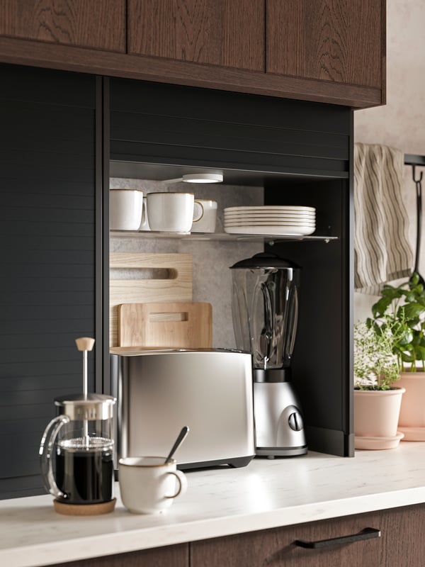 An open black TITTEBO roll-front cabient for small appliances showing a toaster, a blender and two cutting boards inside.