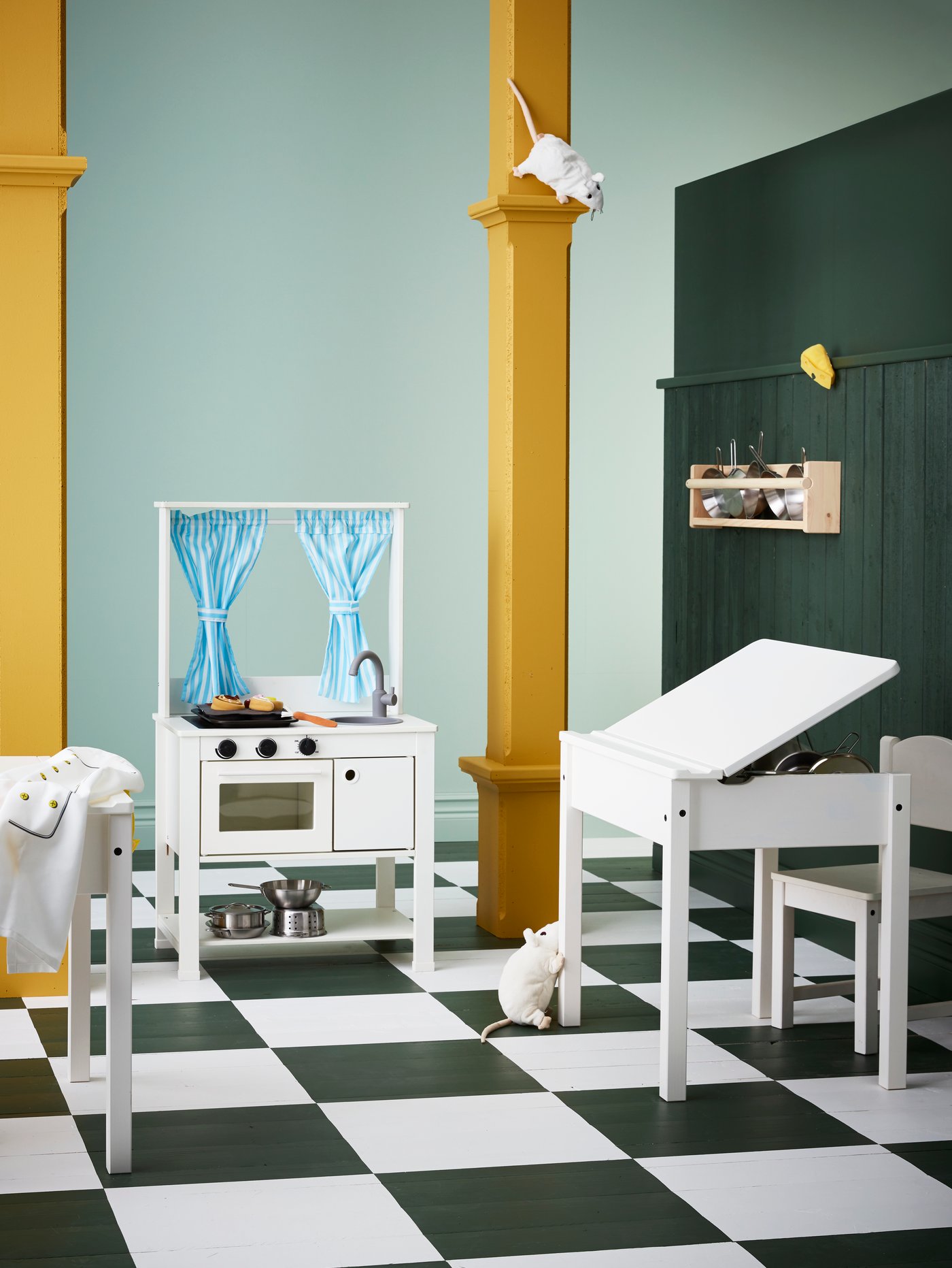 Dos columnas sobre un suelo de cuadros blancos y negros con una cocina de juguete con cortinas, un escritorio infantil y una solución de almacenaje de pared.