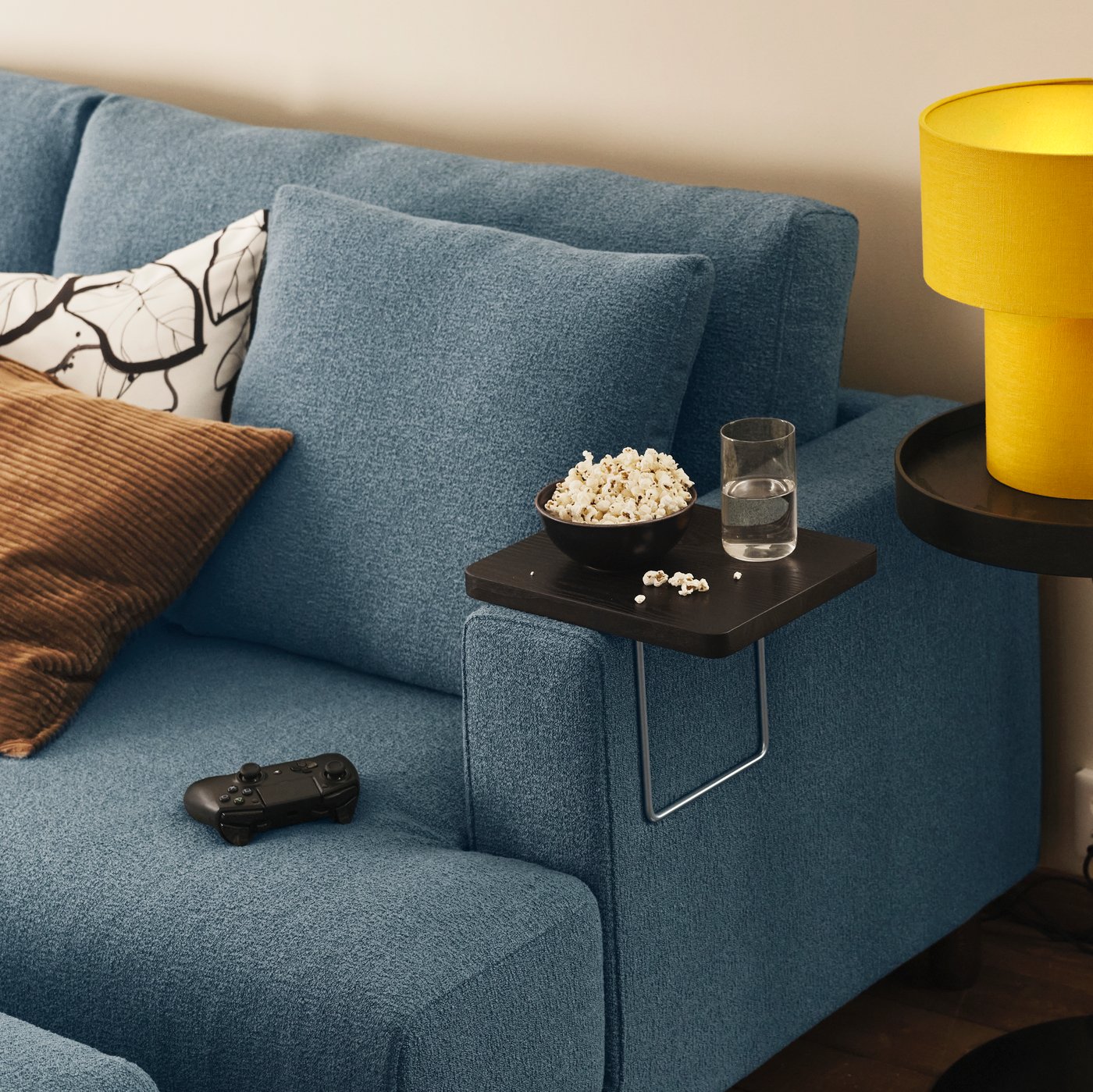 Un plateau d'accoudoir TRANERED, sur lequel sont posés des snacks et un verre, repose sur l'accoudoir d'un canapé modulable UPPÅKRA 4,5 places de couleur gris-bleu foncé.