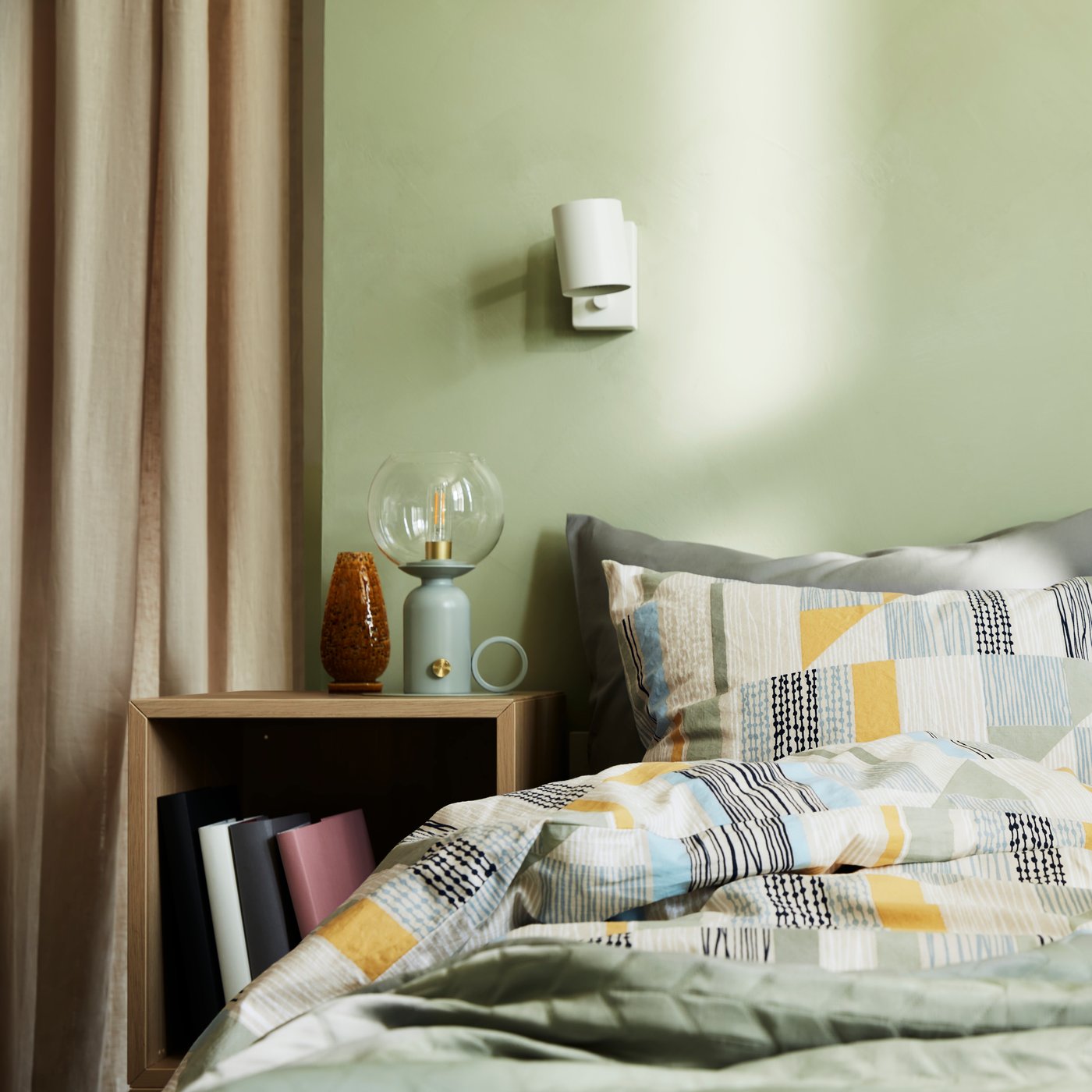 A double bed made with a quilt cover in an abstract pattern in green, yellow, black, beige and blue, and other green bedding.