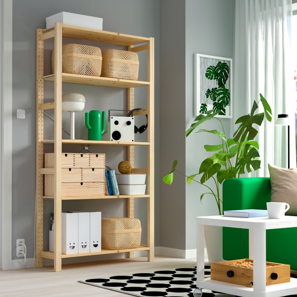 A stylish living room featuring a wooden shelf IVAR with decorative items, plants, and a green sofa beside a white coffee table on a patterned rug.