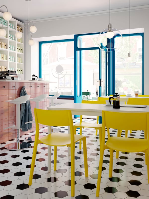 An airy coffee-bar interior with white JANINGE bar stools by a counter and yellow JANINGE chairs at white TOMMARYD tables.