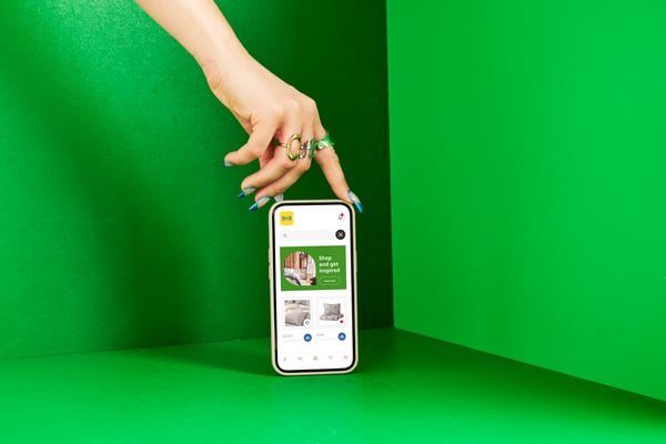 A smartphone is standing upright against a green background; above it, a hand can be seen holding it elegantly.