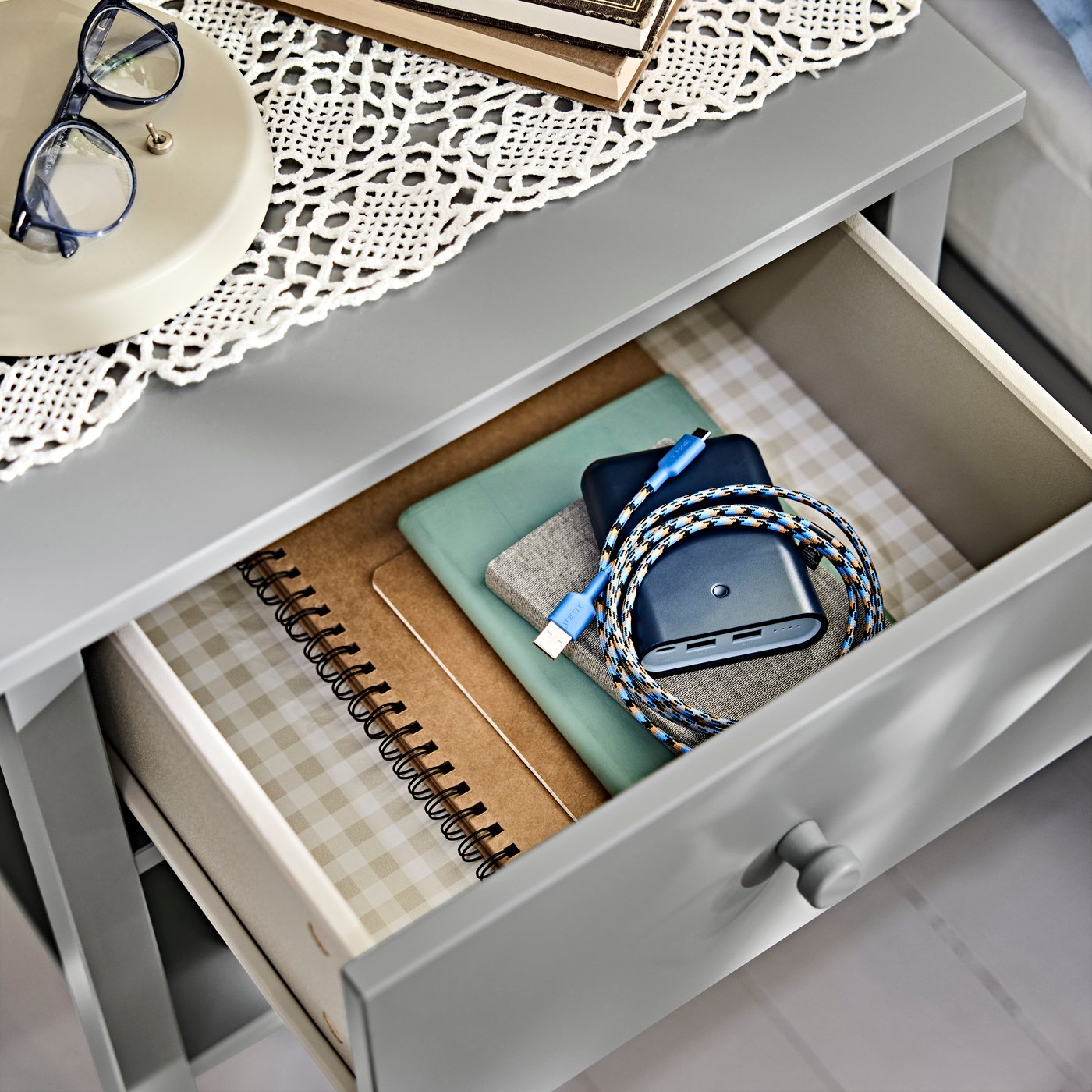 An open drawer containing the VARMFRONT power bank along with notebooks and small accessories inside the bedside table.